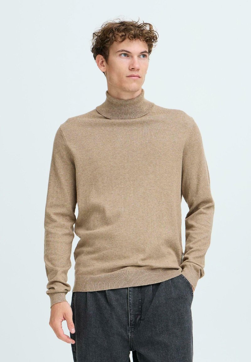 Beige garbónyakú pulóver puha kötött anyagból, karcsú szabással és bordázott mandzsettával, sötét, laza szabású nadrággal párosítva.