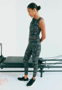 Top corto atletico a fantasia nera e leggings a vita alta, con un design geometrico. Abbinato a scarpe da corsa nere, su attrezzatura da esercizio.