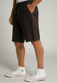 Brune shorts med elastisk taljehæk og snor, med sidelommer. Båret med hvide høj-top sneakers. Glat stofstruktur.
