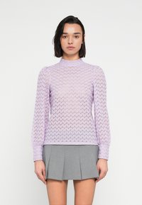 Μπλούζα από πλεκτό ύφασμα σε λιλά απόχρωση με μακριά μανίκια, διακοσμημένη με ζιγκ-ζαγκ μοτίβο και ψηλό λαιμόκοψη. Συνδυασμένη με γκρι φούστα με πιέτες.