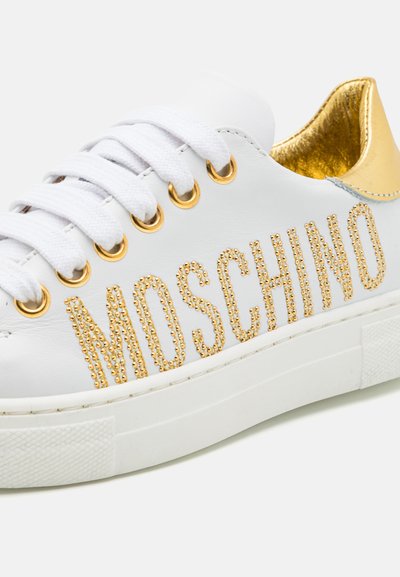 Balti odiniai sportbačiai su auksiniais akcentais, su užrašu "MOSCHINO" auksinėmis deimanto formos detalėmis, plokščiu baltu padu ir auksiniu vidiniu pamušalu.
