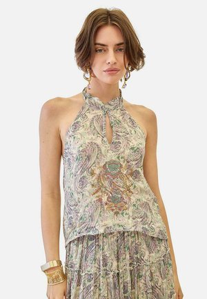 Joven mujer con un top sin mangas de estampado de cachemira y escote con abertura en forma de lágrima, combinado con una falda fluida a juego, complementado con pulseras y pendientes dorados.