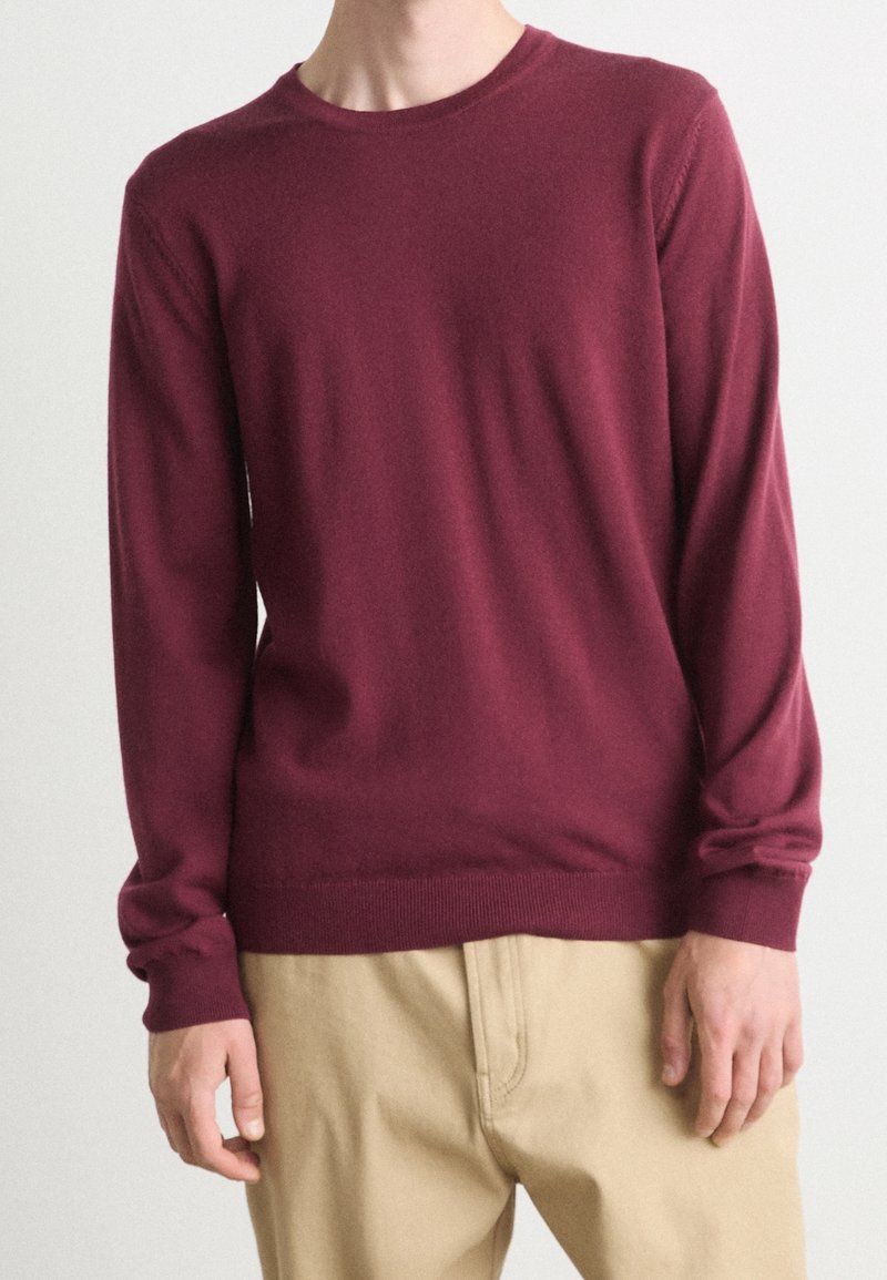 Burgunderfarbener Strickpullover mit langen Ärmeln und rundem Halsausschnitt. Mit gerippten Bündchen und Saum, aus weichem, leichtem Material gefertigt.