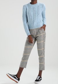 Maglione azzurro chiaro lavorato a maglia con motivo a pizzo aperto, abbinato a pantaloni a quadri bianco e nero e sneakers nere con accenti bianchi.
