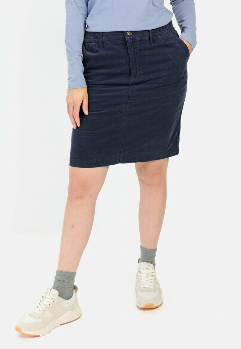 Navy Denimrock im Slim-Fit, mit zwei vorderen Taschen und einem Frontknopfverschluss. Kombiniert mit hellen Sneakers und grauen Socken.