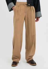 Beige plooibroek met een relaxte pasvorm, gemaakt van zachte stof. Heeft een tailleband met riemlussen en rechte pijpen.