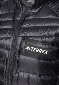 Svart isolerad jacka med kviltat mönster, som har en framzipper, sidoficka och en framträdande "TERREX"-logotyp på bröstet.