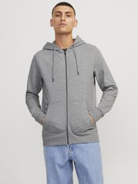 Haut à capuche zippé gris en tissu doux, avec capuche à cordon, poches avant et poignets côtelés, associé à un jean bleu clair.