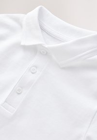 Polo shirt blanche en tissu texturé, avec un col classique et trois boutons au niveau du cou. Design simple et épuré.