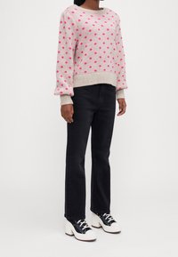 Suéter rosa con estampado de lunares, con cuello redondo y puños acanalados, combinado con jeans negros de pierna recta y zapatillas blancas de plataforma gruesa.