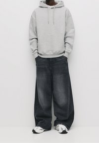 Harmaa huppari, jossa iso etutasku, yhdistetty leveälahkeisiin tummansinisiin farkkuihin ja hopeisiin urheilujalkineisiin. Sileä kangaspinta.