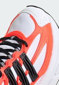 Pantof sport cu un ansamblu superior din plasă albă, accente din plastic roșu, șirete negre și elemente hardware texturate de culoare neagră. Caracteristici un design curbat, aerodinamic.