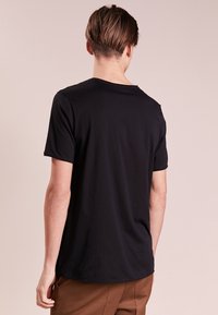 Camiseta negra de manga corta en algodón suave, con un clásico cuello redondo y un ajuste relajado, mostrada desde la parte de atrás.