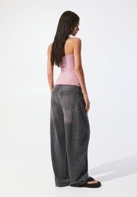 Svetloružový priliehavý top v kombinácii s voľnými čiernymi džínami. Džínsy majú vysoký pás a veľké bočné vrecká. K outfitu patrí aj ploché čierne sandále.