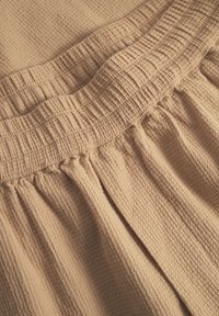 Beige textured fabric with a waffle pattern. Features an elastic waistband with gathered detailing and soft, draped folds.