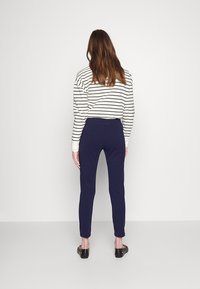 Marinblåa avklippta byxor i mjukt material, i kombination med en långärmad topp i krämfärgat och svart randigt mönster. Slät textur, enkelt design.