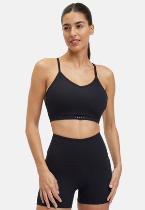 Soutien-gorge de sport noir avec de fines bretelles, un décolleté en V et une bande logo, associé à un short noir taille haute avec une texture lisse.