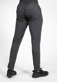 Donkergrijze sportbroeken met een ontspannen pasvorm, elastische tailleband en ritssluiting op de zak, gedragen met zwarte sportschoenen.