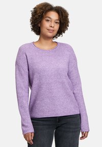 Lila gestrickter Pullover mit einem strukturierten Muster, weitem Rundhalsausschnitt und langen Ärmeln. Kombiniert mit dunklen Jeans für einen lässigen Look.