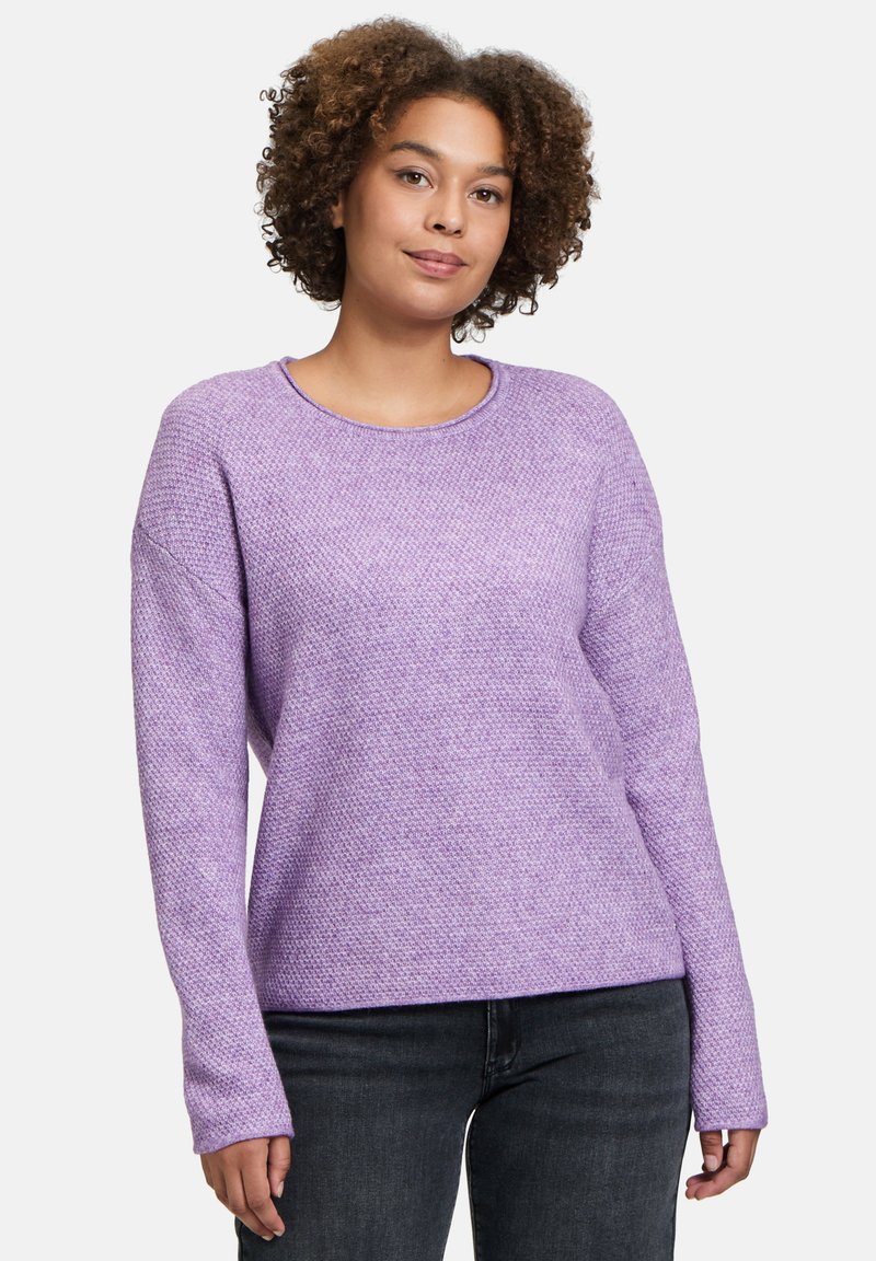 Lila gestrickter Pullover mit einem strukturierten Muster, weitem Rundhalsausschnitt und langen Ärmeln. Kombiniert mit dunklen Jeans für einen lässigen Look.