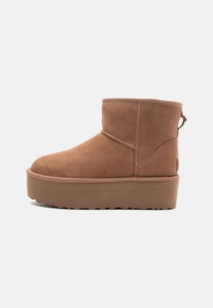 Kurzer brauner Wildleder-Stiefelette mit dickem Plateau-Sohlenprofil und Zuglasche hinten, von der linken Seite auf weißem Hintergrund gesehen.