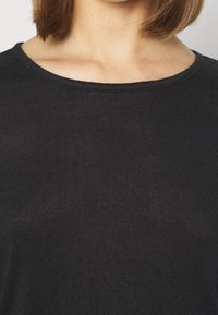 Top nero a costine con scollo rotondo e maniche corte. La texture del tessuto è liscia e il design è semplice e aderente.