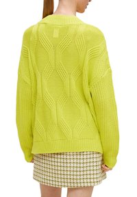 Limettengrüner gestrickter Pullover mit einem strukturierten Wellenmuster und einem gerippten Saum, kombiniert mit einem gemusterten Minirock.