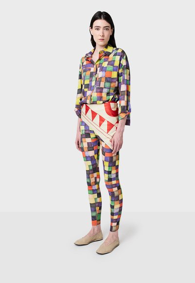 Chemise à carreaux colorée à manches longues, associée à des leggings à motifs présentant un design rouge et crème, et des chaussures slip-on beige clair.