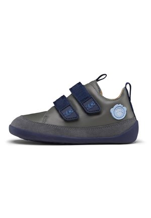 Grauer Lederschuh mit marineblauen Akzenten, zwei Klettverschlüssen und einer Gummisohle. Mit einem runden blauen Logo-Detail an der Seite.