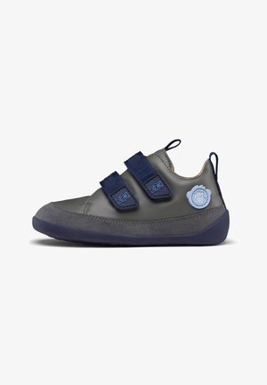 Grauer Lederschuh mit marineblauen Akzenten, zwei Klettverschlüssen und einer Gummisohle. Mit einem runden blauen Logo-Detail an der Seite.