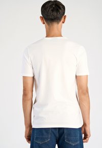 T-shirt bianca a maniche corte con scollo tondo, realizzata in tessuto liscio, indossata con jeans denim blu con tasche posteriori.