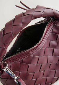 Gewebte bordeauxfarbene Ledertasche mit Reißverschluss, ausgestattet mit einem geflochtenen Griff und Hardware in Silberoptik. Das Innere ist aus schwarzem Stoff.
