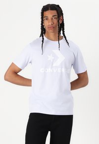 Biela bavlnená tričko s veľkým, centrálne umiestneným, monochromatickým logom Converse a grafikou hviezdy. Krátke rukávy a voľný strih.