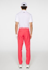 Herenoutfit met een wit poloshirt en felroze op maat gemaakte broeken. De broeken hebben een gestructureerde tailleband en achterzakken, gecombineerd met witte sneakers.
