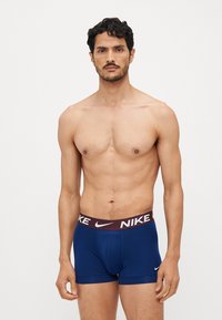 Tamno plave bokserice s bordo elastičnom trakom koja sadrži bijeli "NIKE" logo. Mekana tkanina, prilagođen dizajn, dužina do sredine bedra.