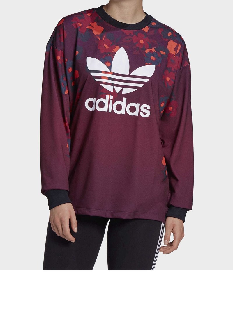 Felpa a maniche lunghe color bordeaux con dettagli floreali, caratterizzata da un grande logo Adidas bianco e bordi neri. Tessuto dalla consistenza liscia.