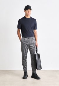 Marineblå kortermet strikket skjorte kombinert med grå stripete bukser, svarte snørebåndsstøvler og en svart tote bag. Minimalistisk design og tekstur.