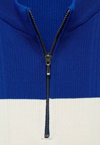 Modra rebrasta zip-up jopica z belo kontrastno horizontalno črto, z kovinsko zadrgo in teksturirano tkanino.