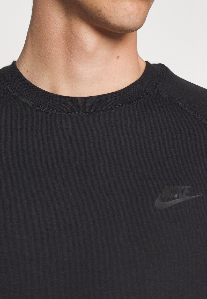 Gros plan sur une personne portant un sweat à capuche noir Nike avec un logo Nike subtil noir sur la poitrine, montrant le cou et une partie du bas du visage.