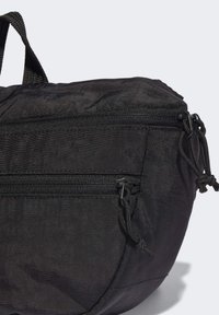 Svart tygväska med två zip-fickor, texturerad yta och justerbara dragsnören för säker stängning. Kompakt rund form.