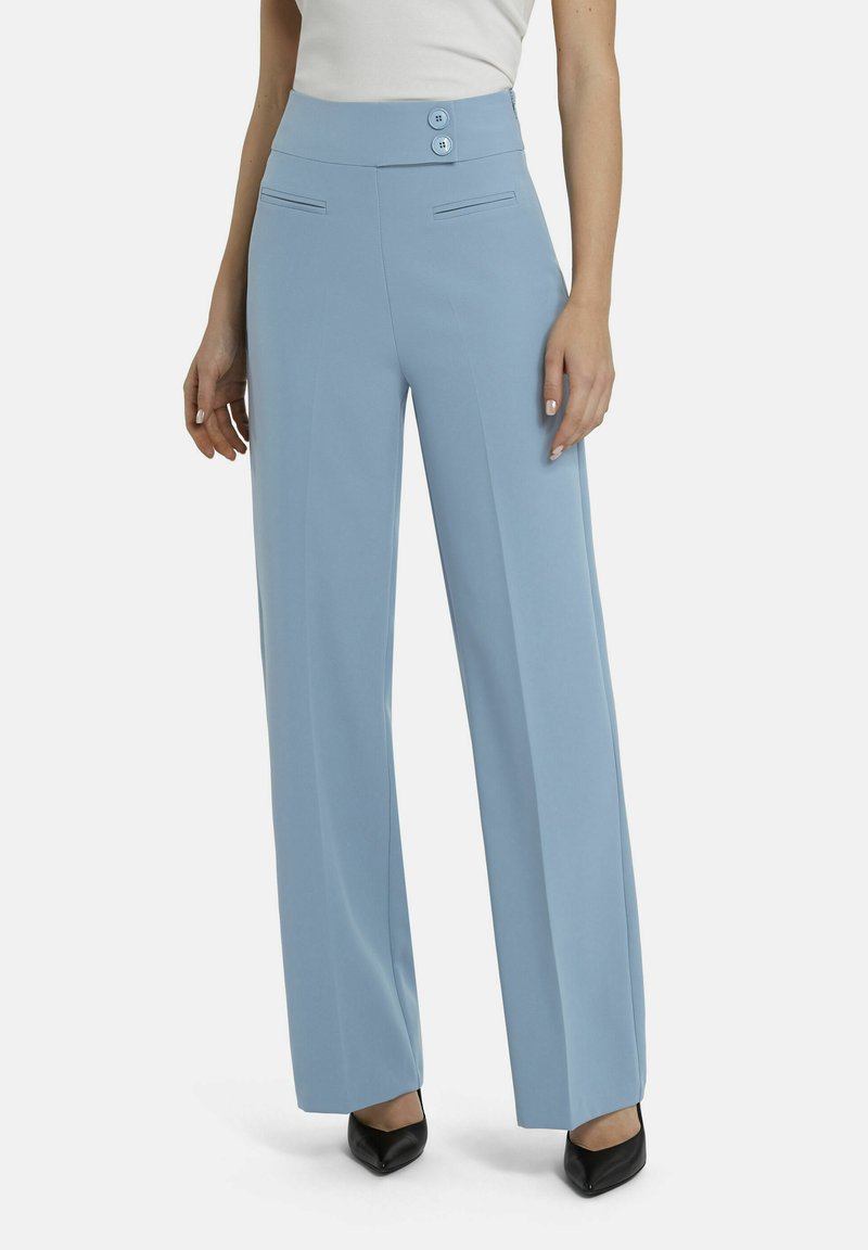 Hellblaue, hoch taillierte, weit geschnittene Hose mit seitlichen Taschen und zwei Knöpfen am Bund, getragen mit schwarzen spitzen Schuhen.