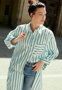 Lyseblå stribet oversized skjorte med en lomme, med hvide og marineblå tynde striber. Bærert over denimjeans, med opsmøgede ærmer.