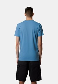 T-shirt a maniche corte e colletto rotondo in cotone azzurro chiaro con una texture liscia, abbinato a pantaloni cargo neri con tasche laterali.