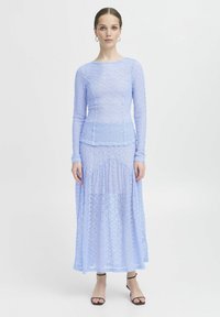 Top a maniche lunghe in pizzo blu chiaro abbinato a una lunga gonna coordinata. Il tessuto è trasparente, con sofisticati motivi floreali e un design fluido.