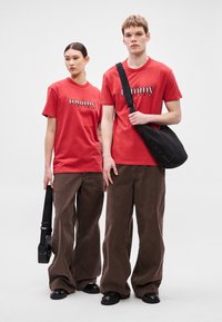 Camisetas de algodón rojo con el logo "tommy jeans", combinadas con pantalones de pana marrones sueltos. Un modelo lleva un bolso cruzado negro.