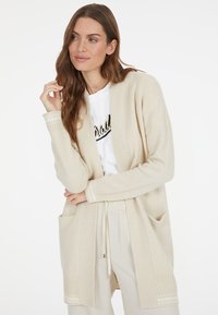 Beiger Cardigan aus weichem Stoff, mit lockerer Passform, langen Ärmeln, seitlichen Taschen und gerippten Details an den Bündchen und dem Saum.
