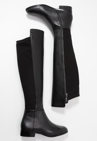 Botas negras hasta la rodilla que combinan cuero y tejido, con un diseño elegante, puntera redondeada, tacón bajo y un detalle de cremallera en el lateral.