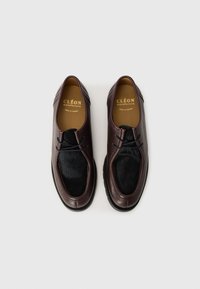 Scarpe di pelle marrone con un morbido accento in pelliccia nera, forma arrotondata, dettagli cuciti e suola in gomma. Nome del marchio impressa sulle solette.