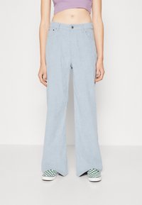 Ljusblå kordflodbyxor med vida ben har en knappstängning, bälteshällor och framfickor. Bärs med gröna rutiga skor i slip-on stil.