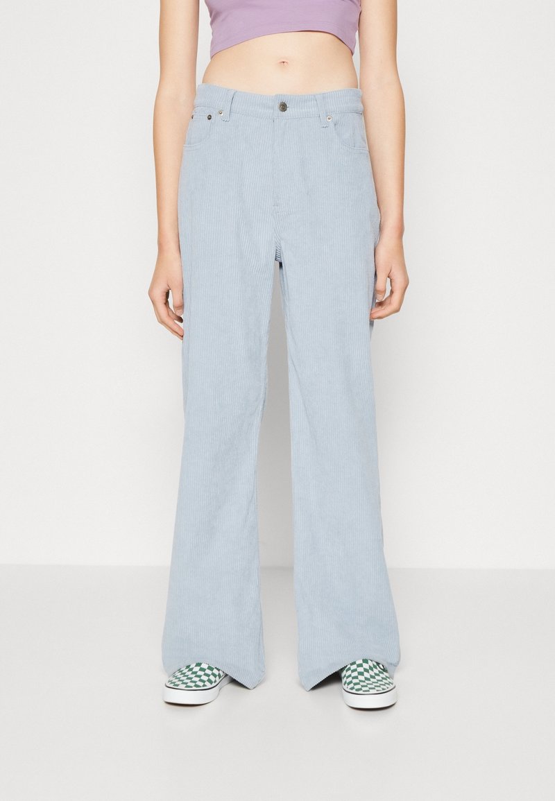 Ljusblå kordflodbyxor med vida ben har en knappstängning, bälteshällor och framfickor. Bärs med gröna rutiga skor i slip-on stil.